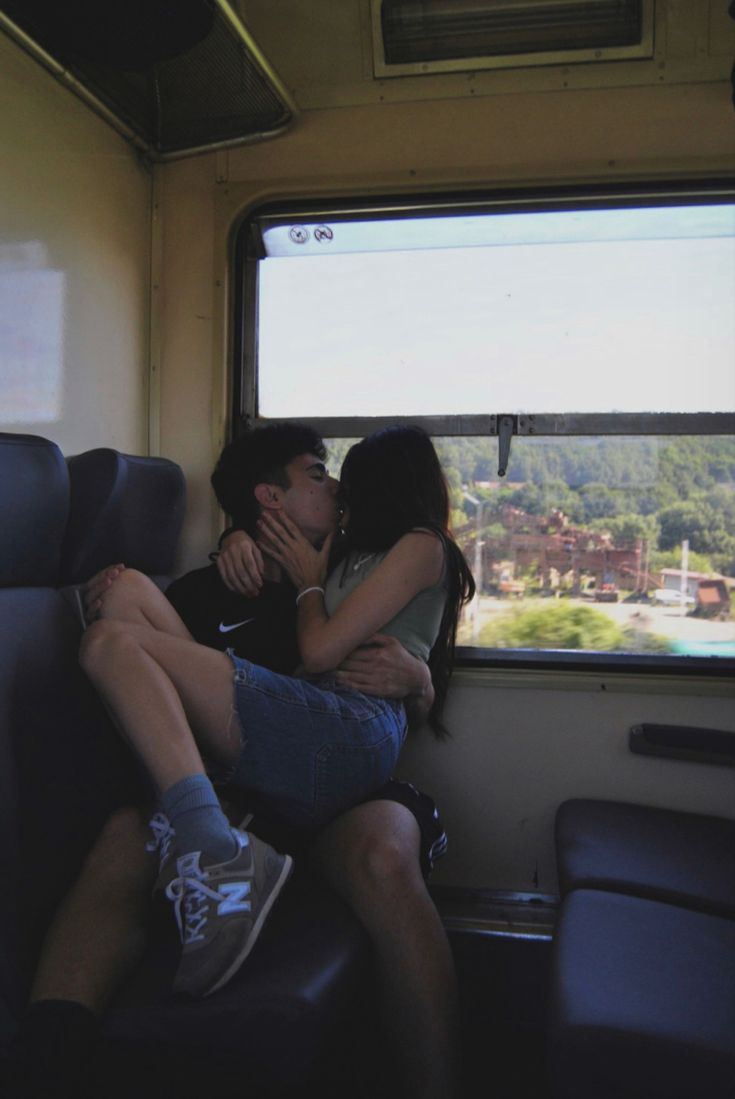 two people sitting on a train with their arms around each other as they look out the window