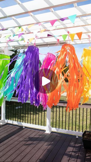 colorful streamers hanging from a white pergolated roof over a wooden deck in front of a fence