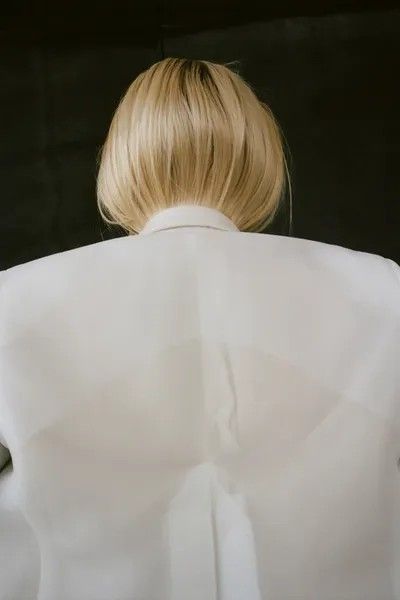 the back of a woman's head with blonde hair in a white shirt and black pants