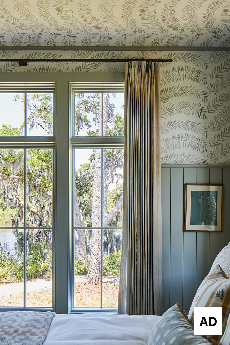 a bed sitting under two windows next to a window covered in curtained drapes