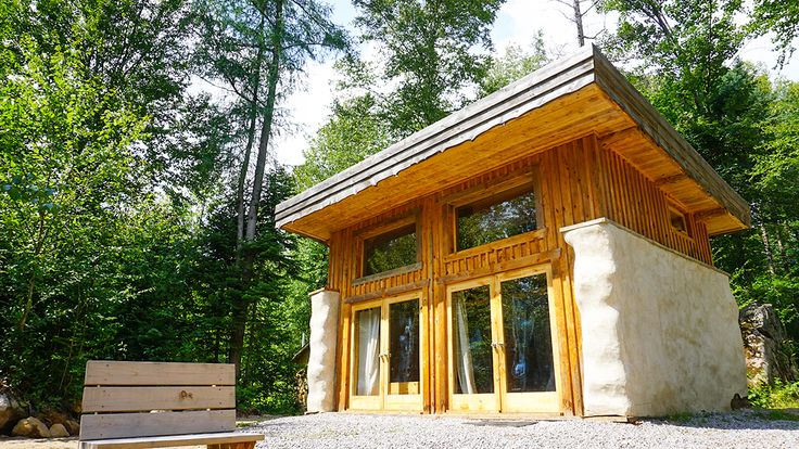 a small wooden building sitting in the middle of a forest next to a park bench