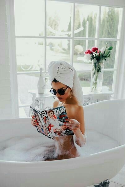 a woman sitting in a bathtub reading a magazine