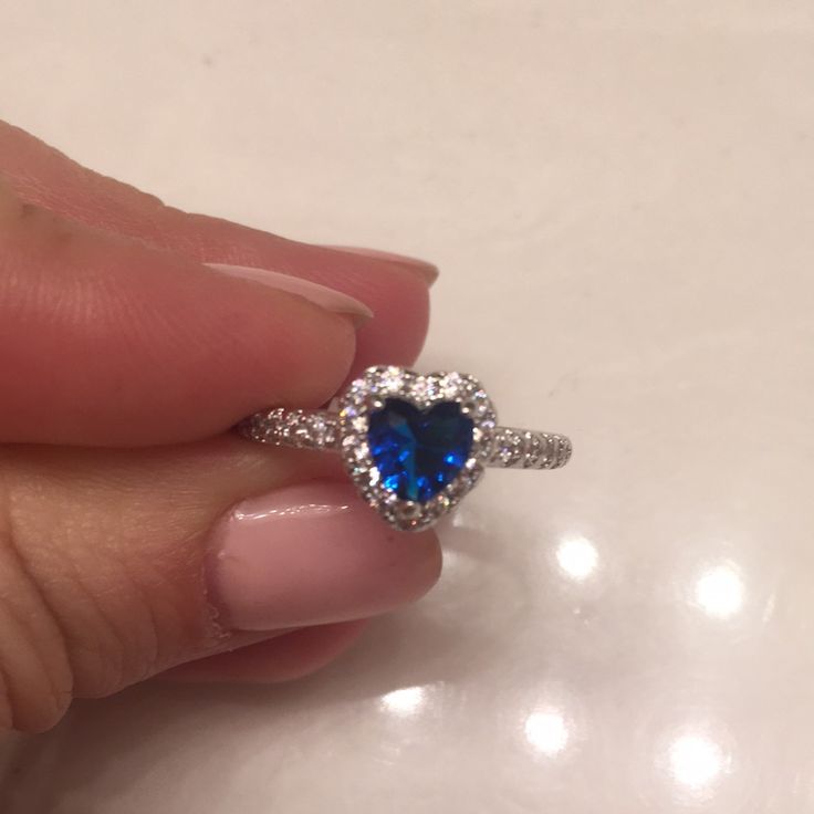 a woman's hand holding an engagement ring with a blue stone in the center