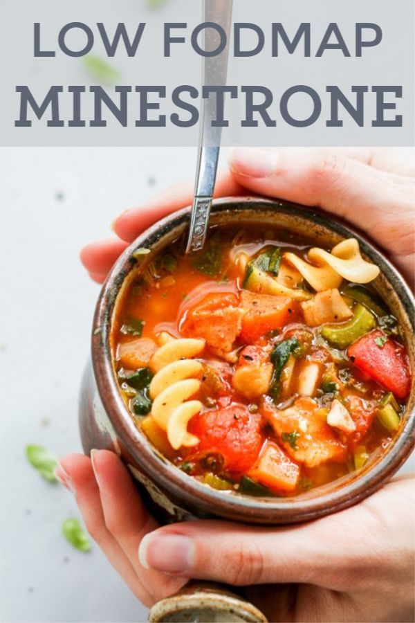 two hands holding a bowl of pasta and vegetable soup with a spoon in the bowl