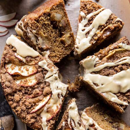 an apple crumb cake with white icing is cut into slices and sits on a cutting board