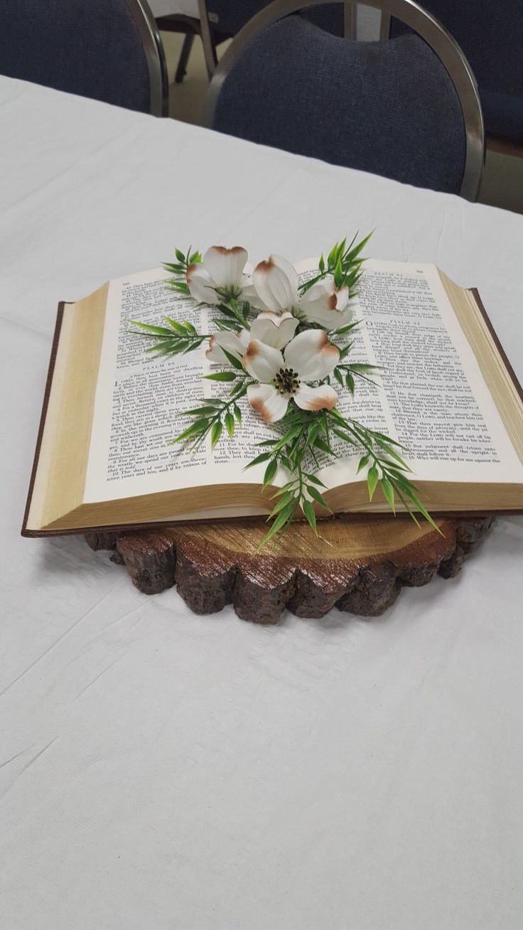 an open book sitting on top of a table with flowers in the middle of it