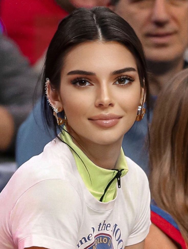 a close up of a person wearing earring's and a crowd behind her