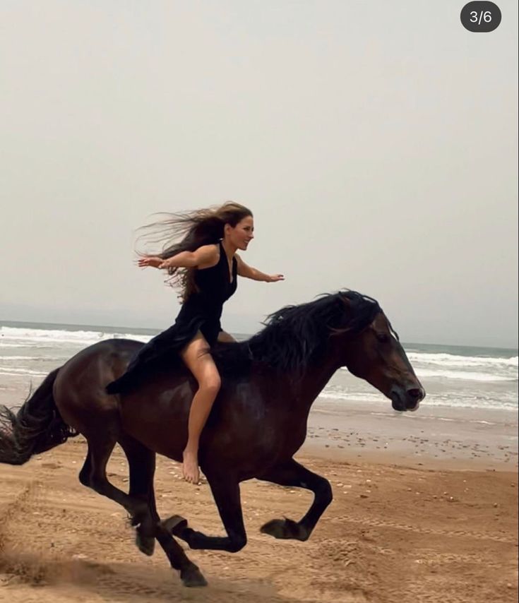 a woman riding on the back of a brown horse down a sandy beach next to the ocean