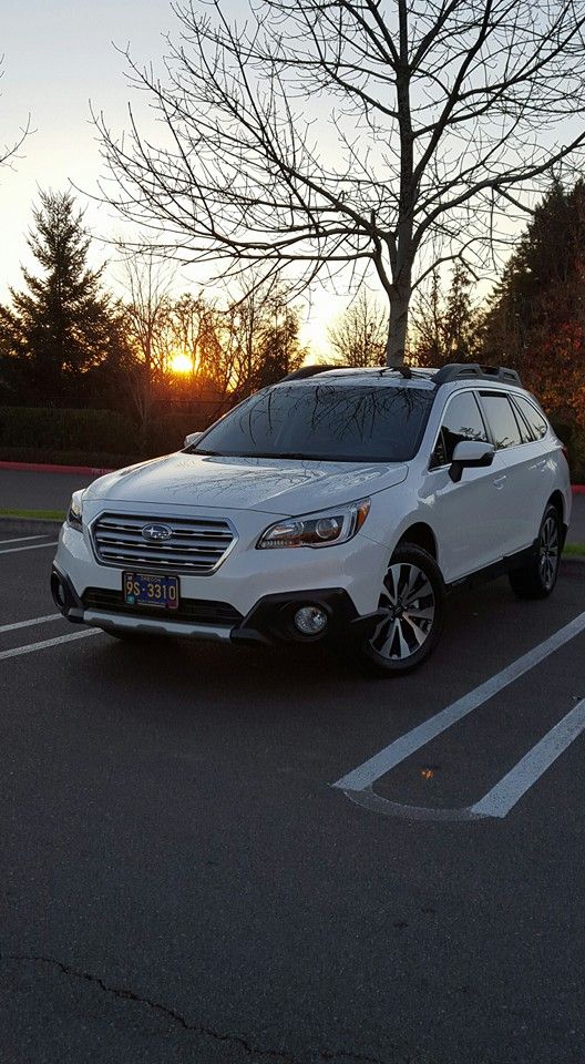 a white subarunt is parked in a parking lot at sunset with the sun behind it