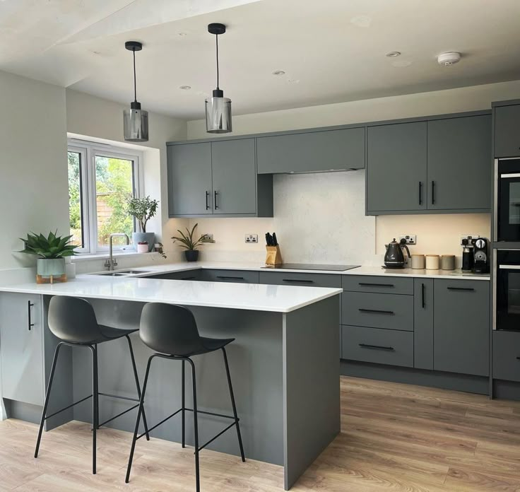 a kitchen with grey cabinets and white counter tops, two bar stools in front of the island