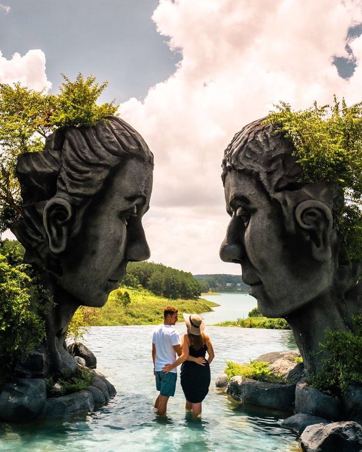 two people are standing in the water between two statues that look like they're facing each other