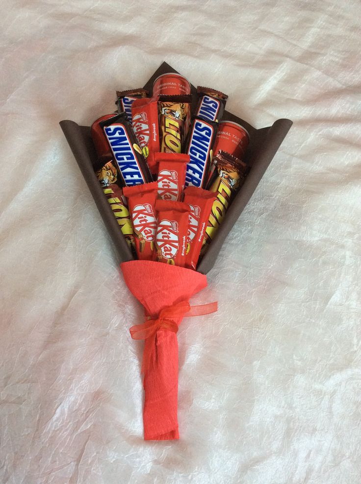 a bouquet of candy wrapped in red ribbon on top of a white sheeted bed