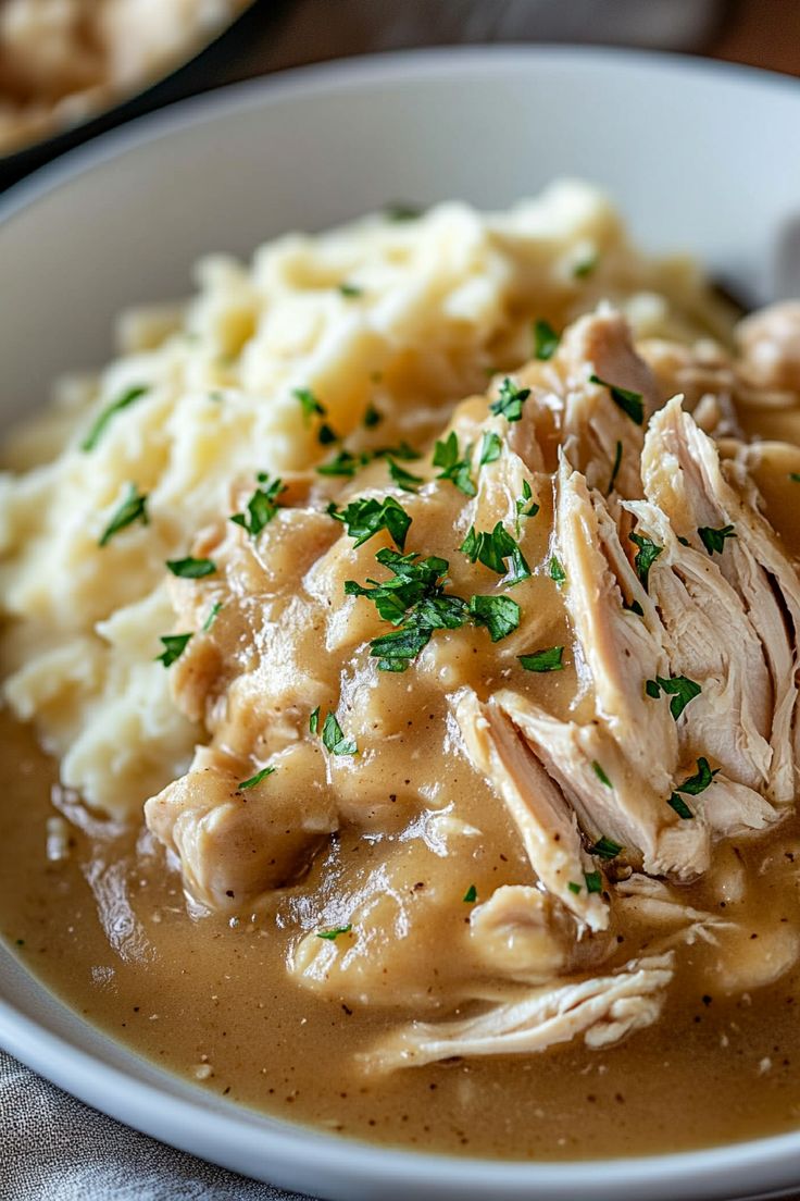 a white bowl filled with meat and gravy on top of mashed potatoes