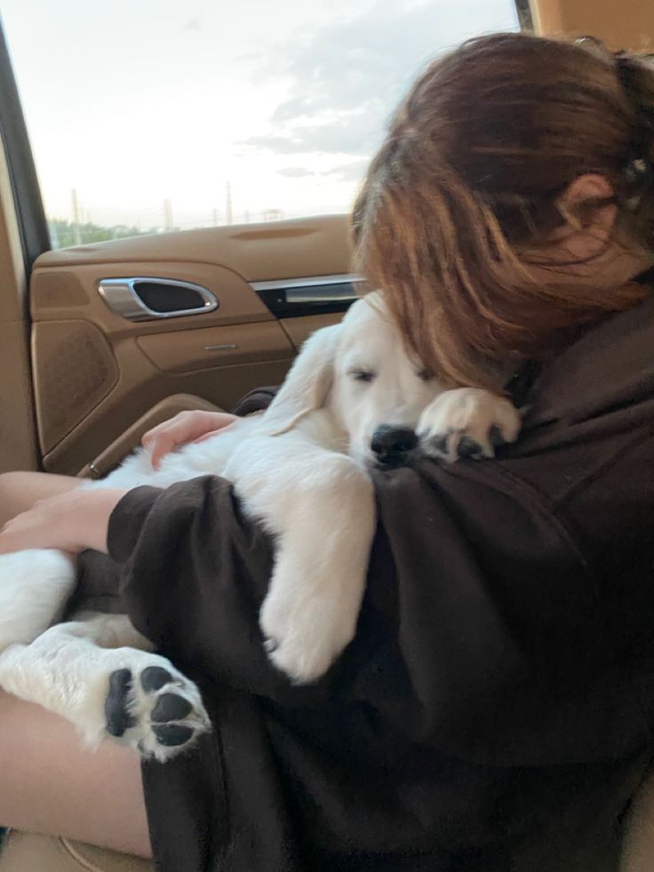 a woman holding a dog in her arms while sitting in the back seat of a car