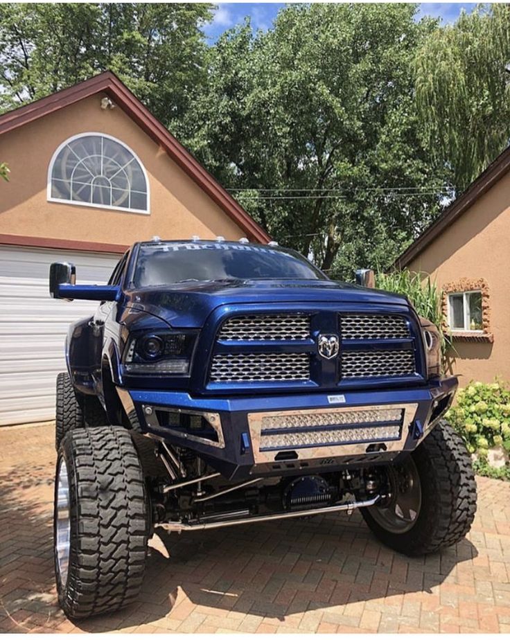 a large blue truck parked in front of a house with big tires on it's sides