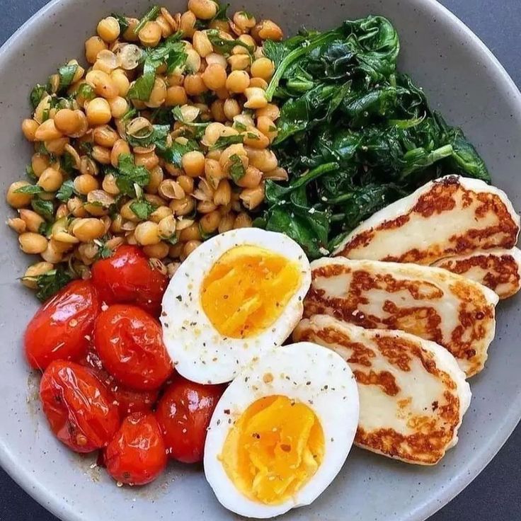 a white plate topped with eggs, tomatoes and spinach next to chickpeas