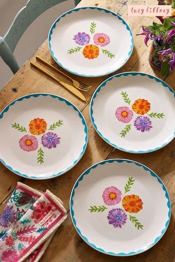 four plates with flowers painted on them sitting on a table