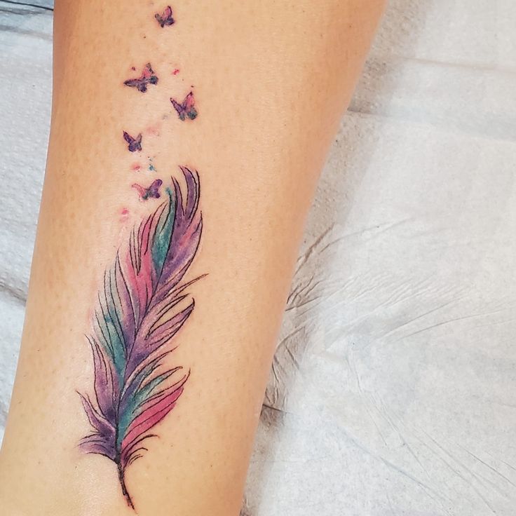 a woman's foot with a colorful feather and butterflies tattoo on the side of her leg