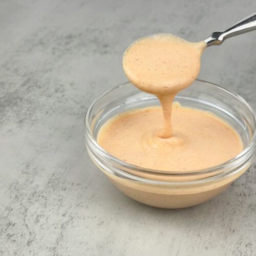 a glass bowl filled with sauce and a spoon in it, on top of a table