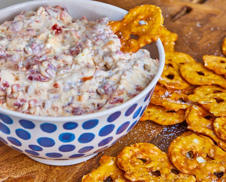 a bowl filled with dip next to crackers and pretzels