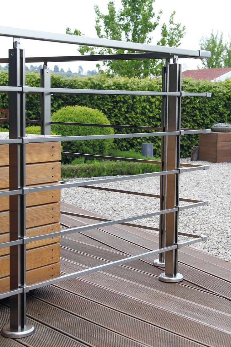 a wooden bench sitting on top of a wooden floor next to a metal fence and shrubbery