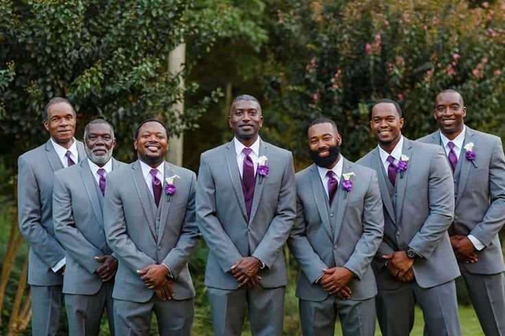 a group of men standing next to each other wearing suits and ties with purple flowers on their lapels