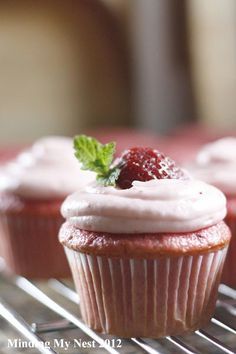 two cupcakes with frosting and a strawberry on top sitting on a cooling rack