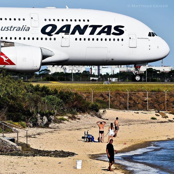 an airplane is flying over the beach with people walking on the sand and in the water