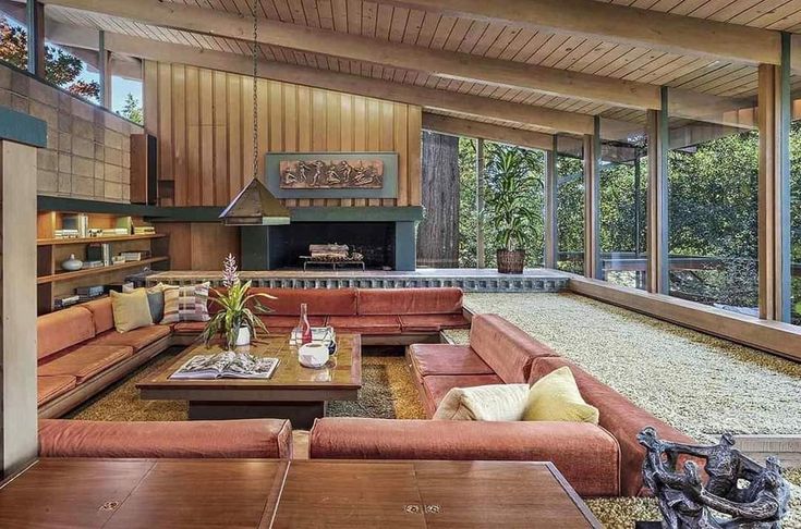 a living room with couches, tables and windows looking out onto the forest outside