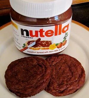 a white plate topped with two cookies next to a jar of nutella