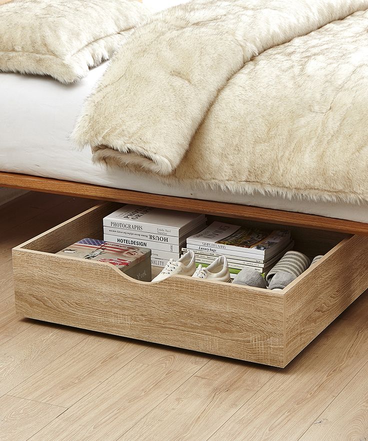 a bed with a white fur blanket on top of it next to a wooden drawer