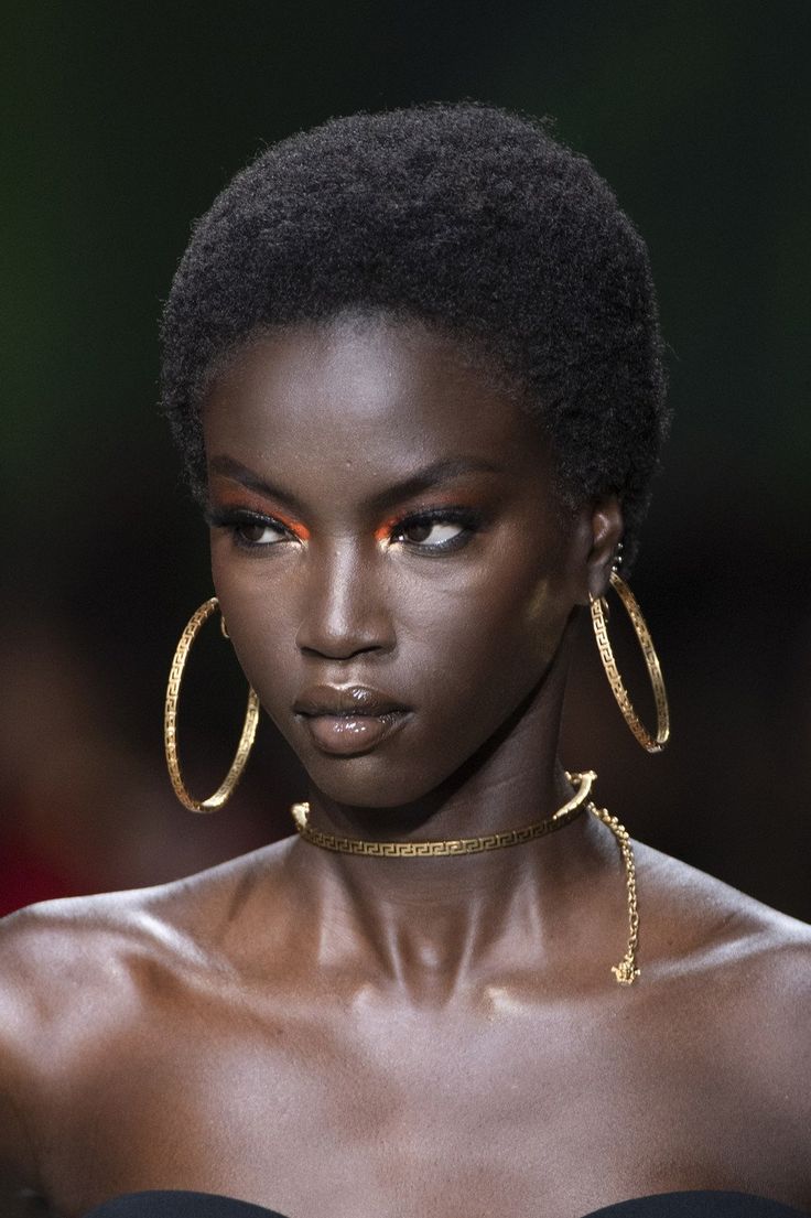 a model with dark skin and gold hoop earrings on her head, looking at the camera