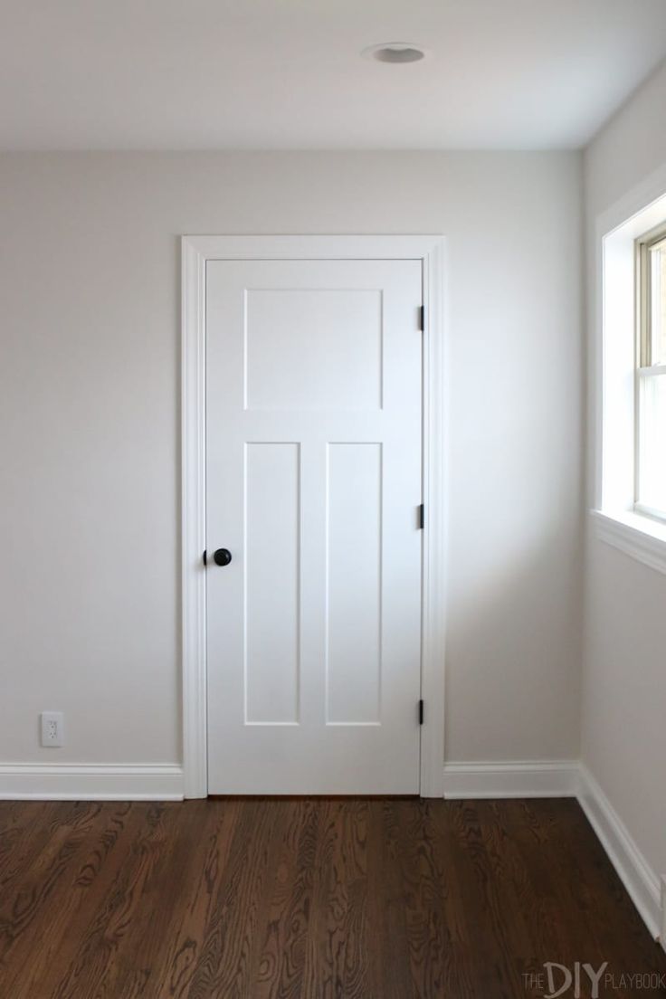 an empty room with a white door and wood floors in the corner is seen from across the room