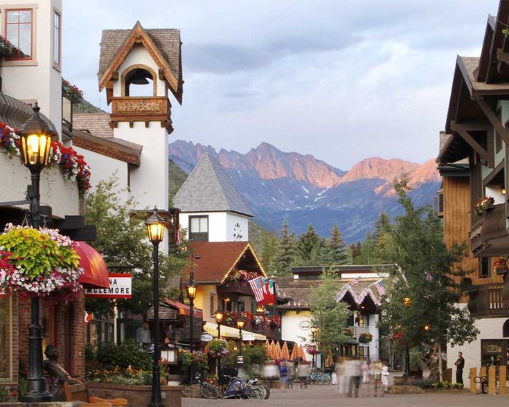 people are walking down the street in front of buildings with mountains in the back ground