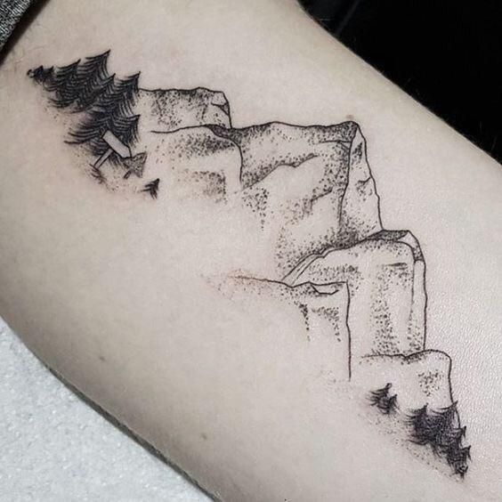 a black and white photo of a man's arm with a mountain scene tattoo on it