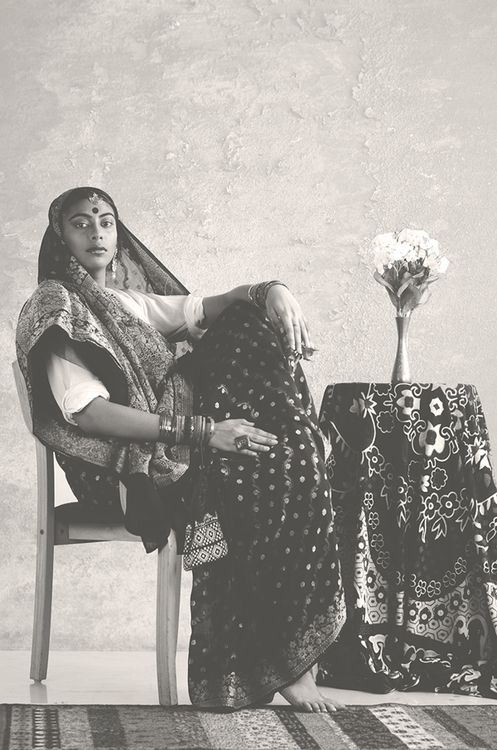 a woman sitting in a chair next to a table with a vase on top of it