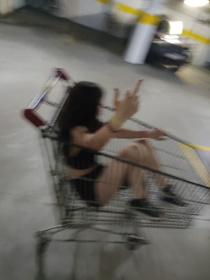 a woman sitting in a shopping cart with her hand up to the side and another person standing behind it