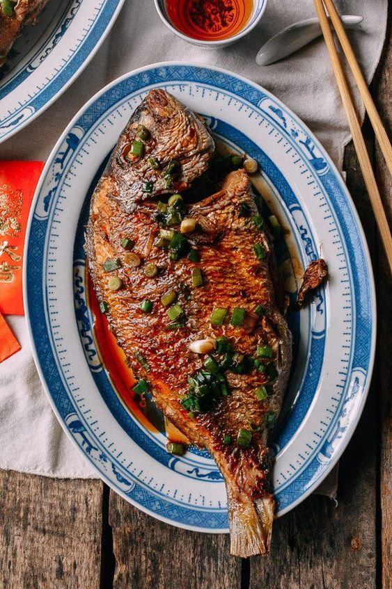 two plates with food on them and chopsticks next to one plate that has fish