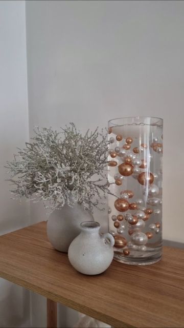 two vases are sitting on a table with some flowers in them and one is filled with balls