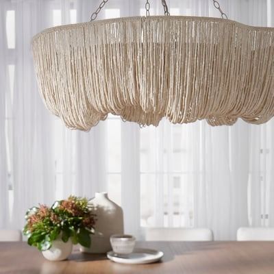 a chandelier hanging over a wooden table in a room with white drapes