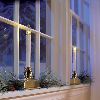 two candles sitting on top of a mantle in front of a window with evergreen branches and pine cones