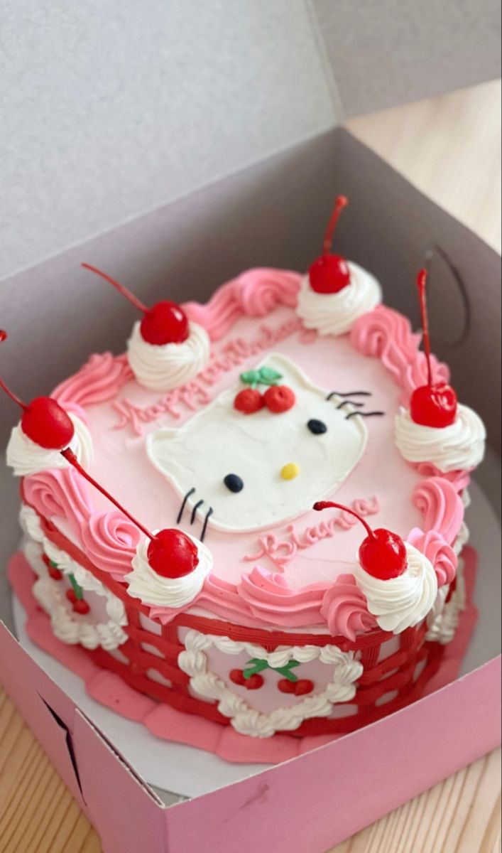 a hello kitty cake in a pink box with cherries on the top and one cherry on the side