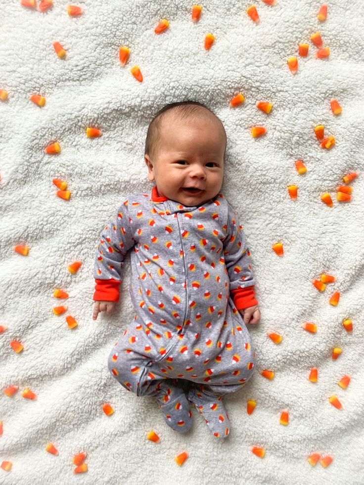 a baby laying on top of a blanket covered in candy corn kernels and smiling at the camera