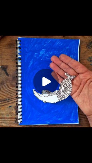 a hand holding a piece of paper next to a spiral notebook with an ornament on it