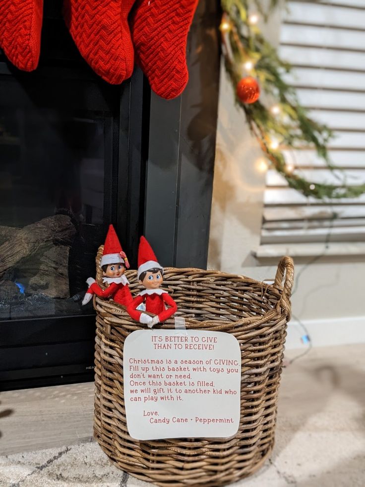 two elfs sitting in a basket next to a fireplace