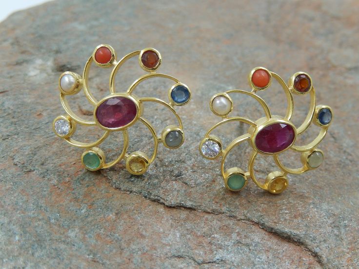 "About Earrings Stud: Dimension: 2.25 cm wide Available in Silver 925, Silver Gold Plated 925, 14k Gold & 18k Gold A \"Navratan\" ring, also known as a Navaratna or Nine-Gemstone ring, is a piece of jewelry that incorporates nine different gemstones, each representing one of the nine celestial bodies in Vedic astrology. The concept of the Navratan ring originates from ancient Indian astrology and is believed to bring astrological benefits and balance to the wearer. The nine gemstones typically i Navarathna Ear Rings, Navratan Earrings, Navratna Rings Gold, Navratna Ring, Navratan Ring, Navratna Earrings Gold, Navaratna Studs Gold, Navratna Earrings, Navratna Ear Studs