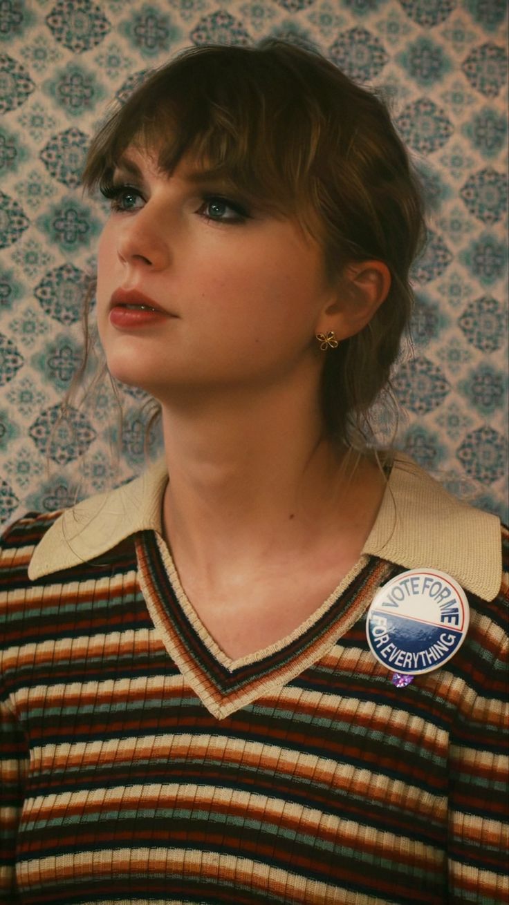 a young woman wearing a striped sweater with a button on her left shoulder and an embellished badge on her right chest