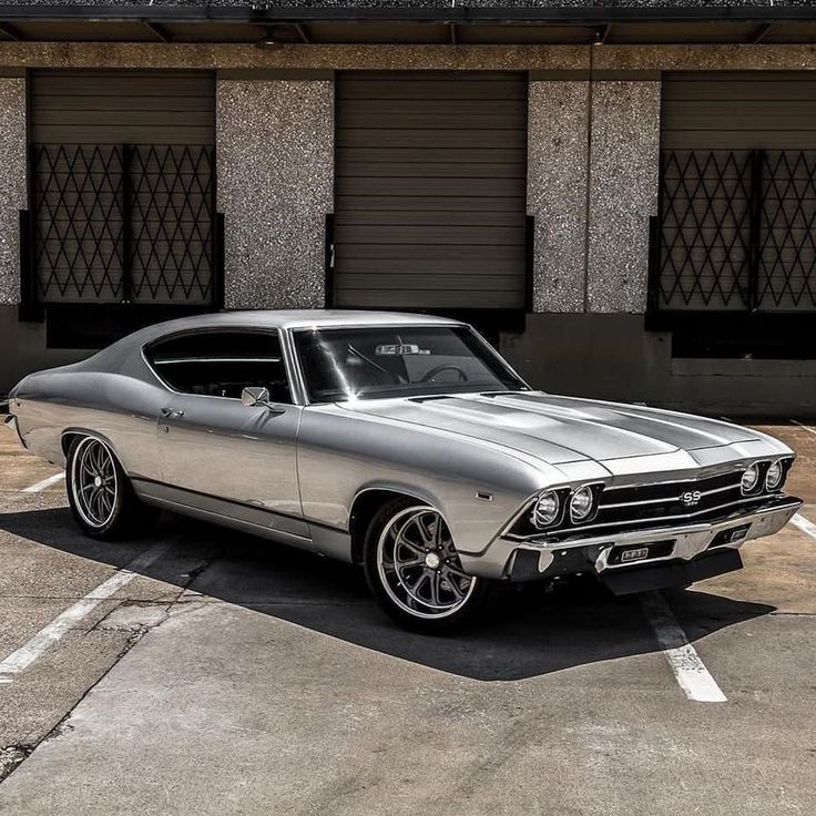 a silver muscle car parked in a parking lot next to a building with black shutters