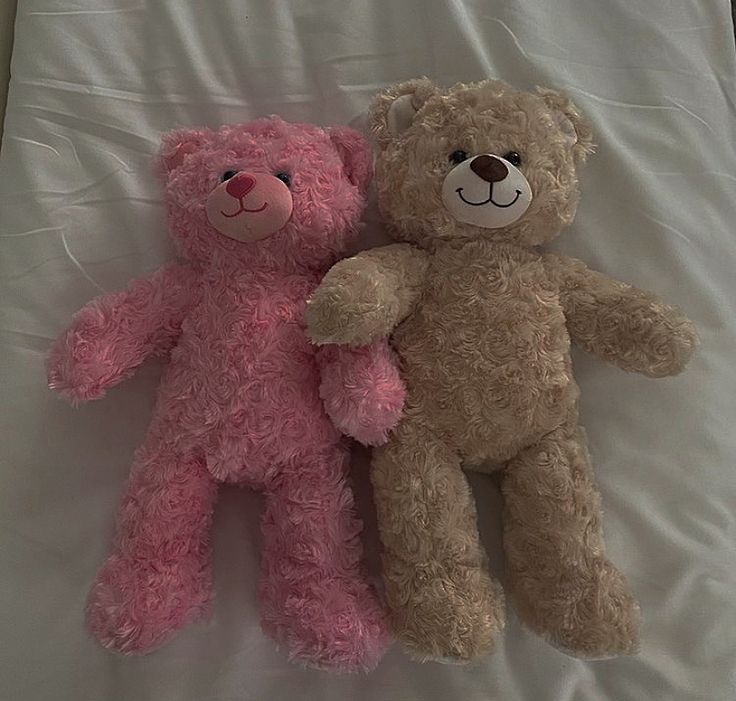 two teddy bears laying next to each other on a bed