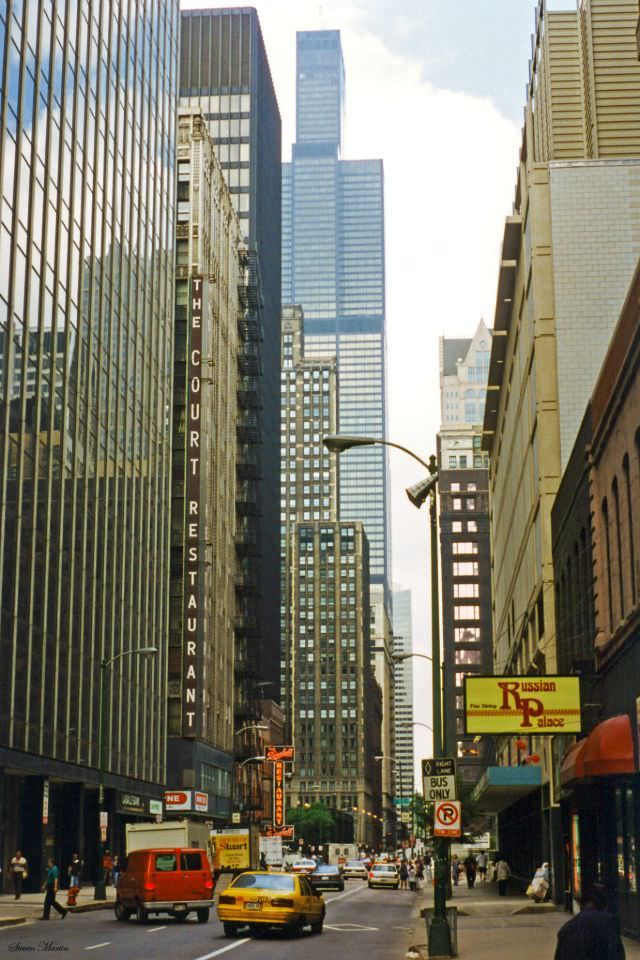 a city street filled with lots of tall buildings and people walking on the side walk